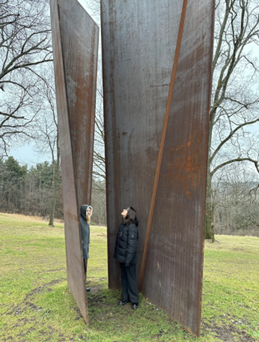 Two people stand within large, upright metal panels that are situated outdoors