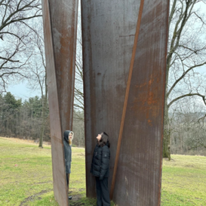 Two people stand within large, upright metal panels that are situated outdoors
